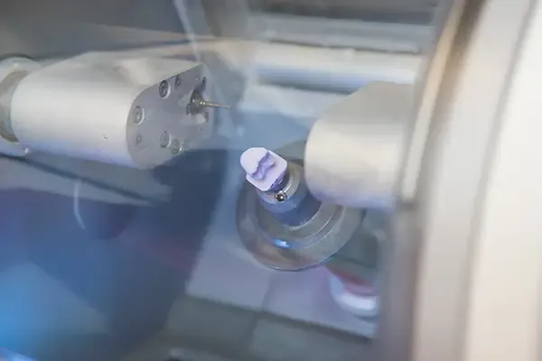 A close-up view of a machine milling a dental crown from a ceramic block for same-day restoration.
