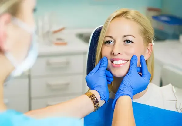 A dentist wearing blue gloves checking a female patient’s smile in a dental clinic, showcasing professional dental care.