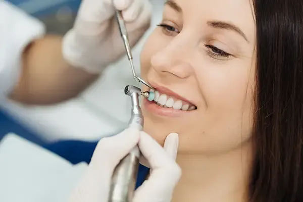 A woman grinning while a dentist holds up a mirror and inspects her healthy teeth after a thorough dental cleaning.
