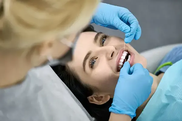 A hygienist flosses a female [patient's newly cleaned teeth at the end of her dental visit.