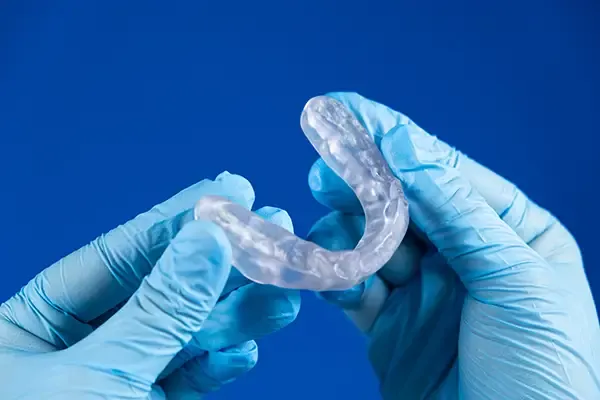 Dentist with gloved hands holding a clear mouth guard, showcasing quality dental appliance care.