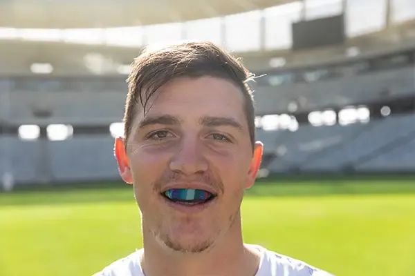 A smiling male rugby player wearing a protective sports guard while practicing.