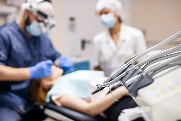 A close-up view of dental tools with a dentist and assistant working on a patient in the background during a dental surgery.