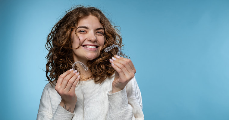 A woman is holding Invisalign® clear aligners and smiling