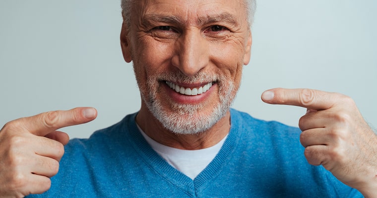 An older man smiling and pointing at her smile